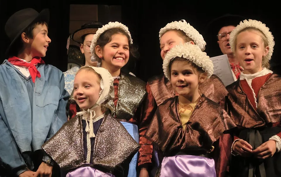 Enfants en costumes savoyards traditionnels et coiffes de dentelle chantant sur scène, spectacle en patois