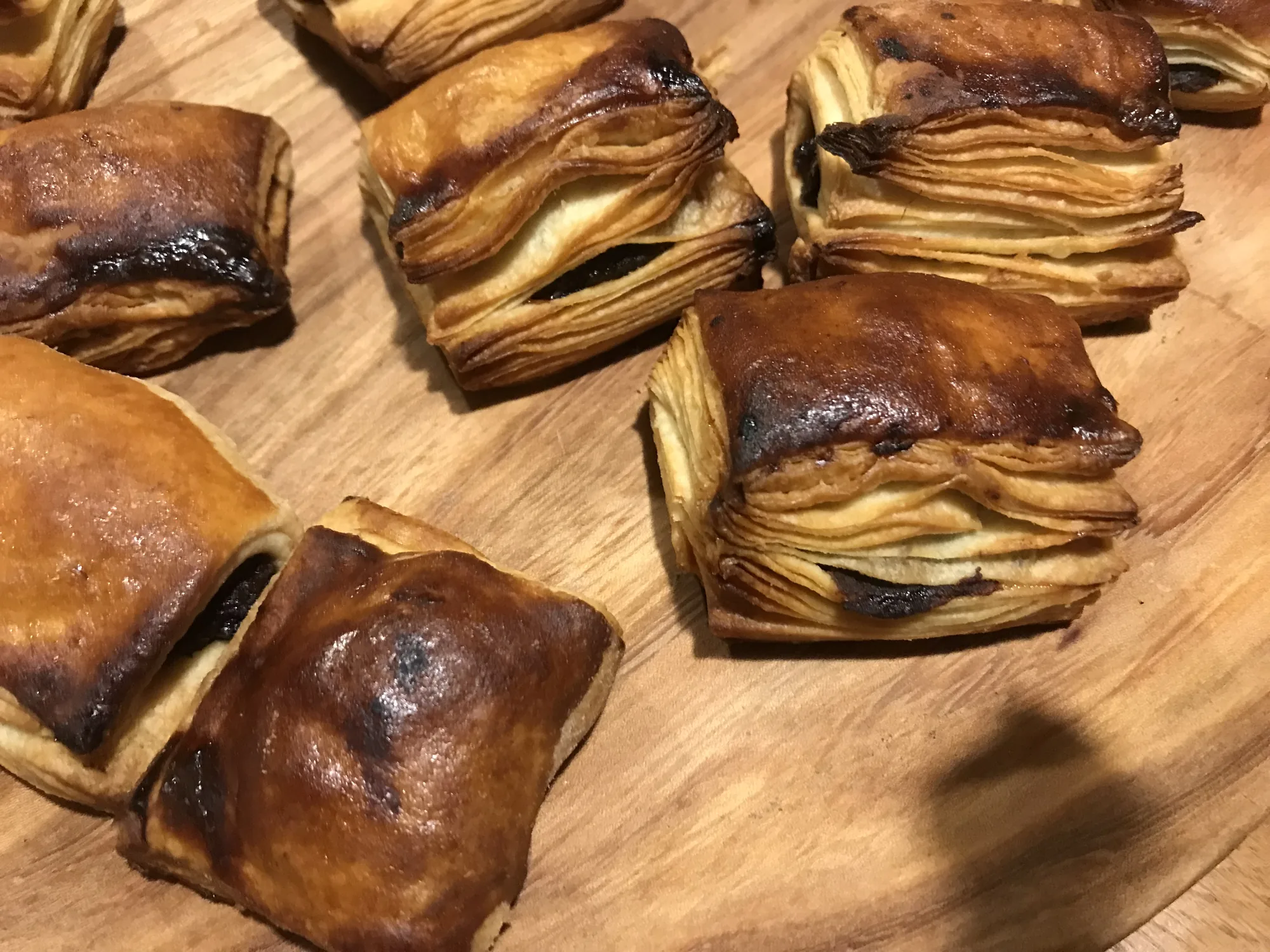 Rissoles de Noël, posées sur une planche en bois. On voit leurs fines couches de pâte et leur garniture.